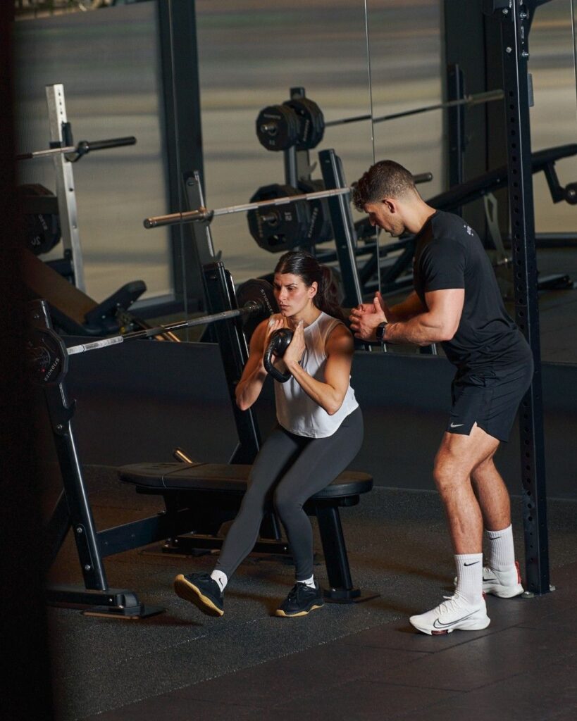 Personal fitness trainer guiding a woman through strength training exercise in gym